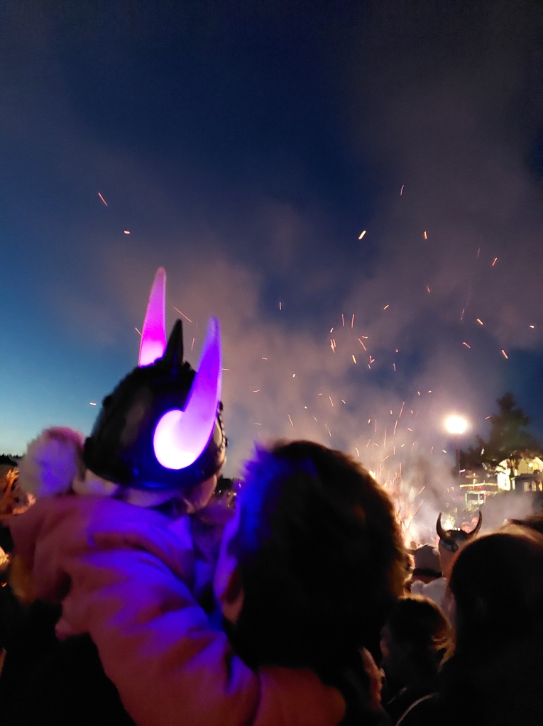 A small girl in a lit-up Viking helmet watches the bonfire